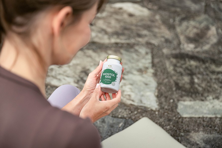 Kvinna sitter på en yogamatta och håller en burk Healthwell Inositol 1000 i händerna.