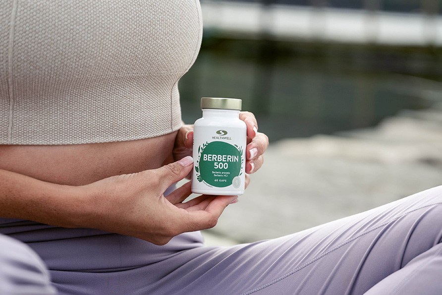 Kvinna håller en burk Healthwell Berberin 500 utomhus vid vattnet.