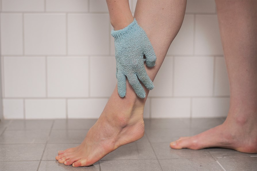 Hand med skrubbvante som peelar ett ben