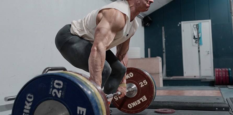 Man som sitter på huk och ska lyfta en skivstång. Man som sitter på huk och ska lyfta en skivstång.