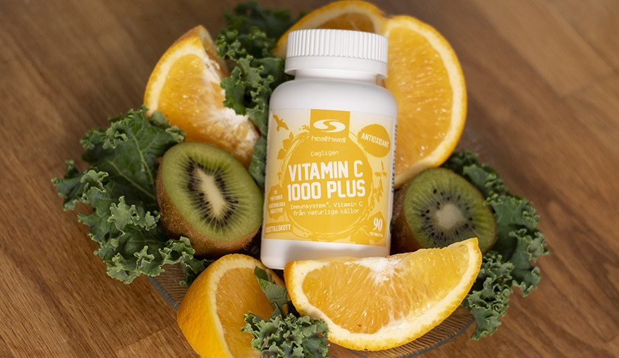 Bild p Vitamin C 1000 Plus p ett bord i en bdd av citroner, kiwi och grnkl.