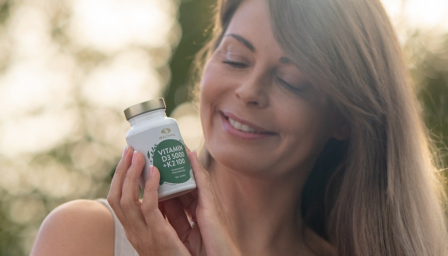 Glad kvinna h�ller i Healthwell Vitamin D3 5000 + K2 100 ute i naturen.