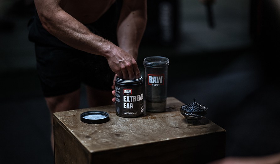 RAW SUPPS Extreme EAA placerad p en box med en shaker bredvid och en person som tar en skopa ur burken.