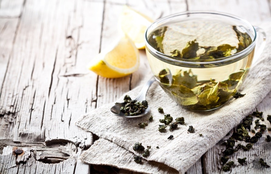 Glaskopp fylld med grnt te. Grnt te utspritt runt koppen, samt en sked och en citron.
