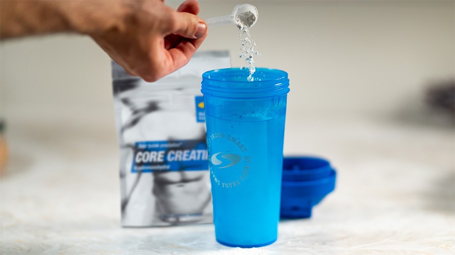 En hand h�ller i en skopa Core Creatine i en bl� shaker. 