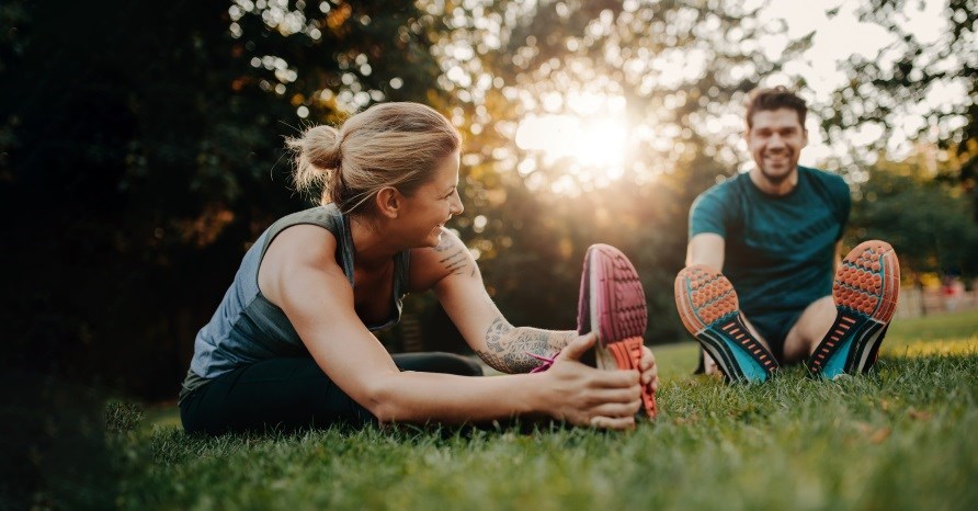 Tjej och kille som sitter på gräset utomhus och stretchar. Tjej och kille som sitter på gräset utomhus och stretchar.
