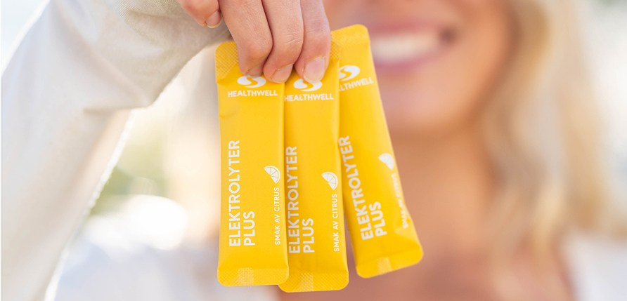 Kvinna håller tre sachetter med Healthwell Elektrolyter Plus.