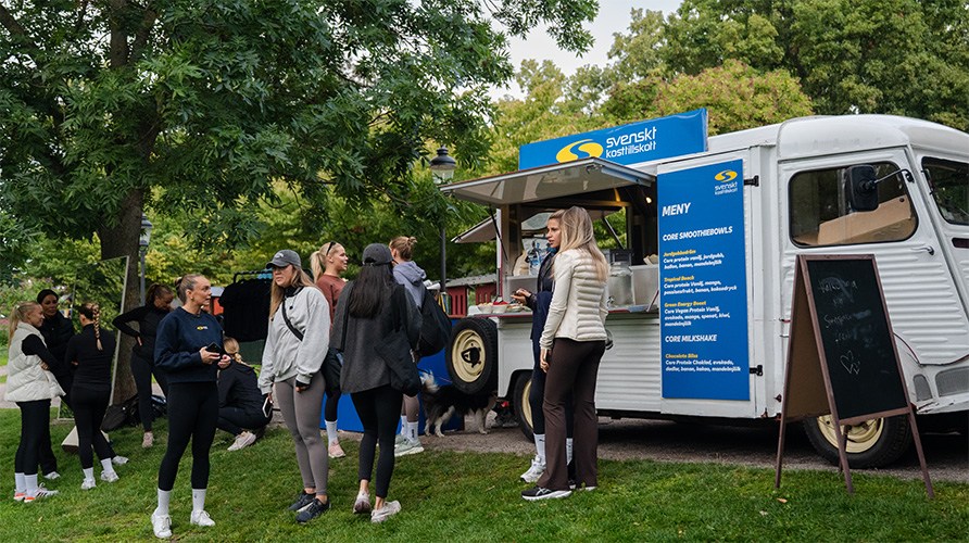 Ett event dr en grupp mnniskor str p en grsmatta bredvid en foodtruck som r mrkt med Svenskt Kosttillskotts logotyp. 