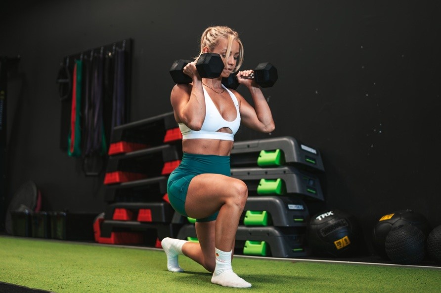 En kvinna g�r utfallsg�ng med hantlar. 