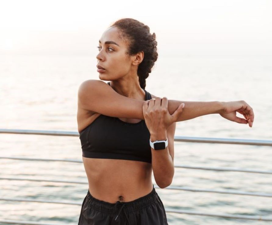 Kvinna i trningsklder som strechar sin arm i utomhusmilj.