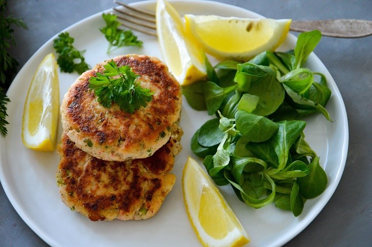 Laxbiffar med machsallad och citron p en vit tallrik.