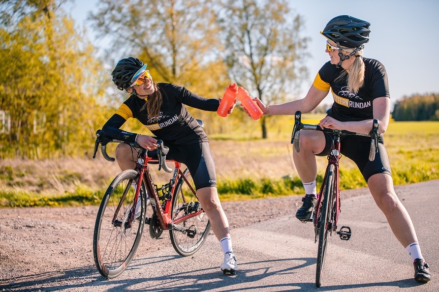 Tv kvinnor utomhud p varsin cykel med en shaker i handen.