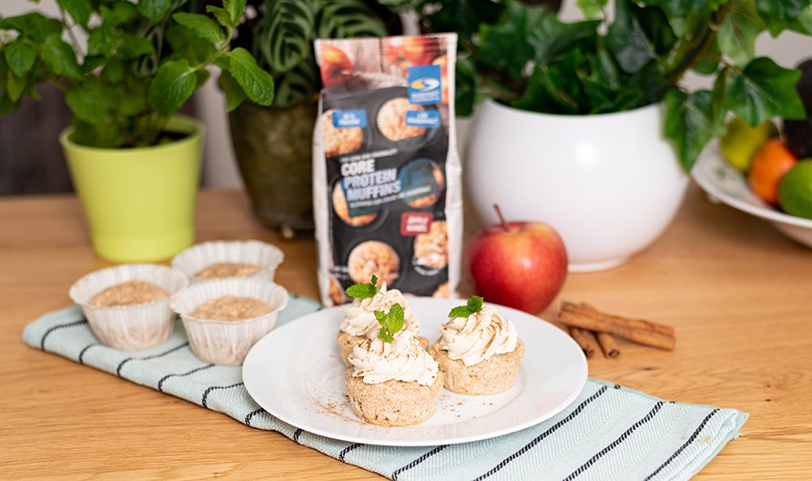 Bakade �ppelmuffins toppade med vanilj och kanelfrosting. Uppdukade p� ett vitt fat med �pple och kanel i bakgrunden.