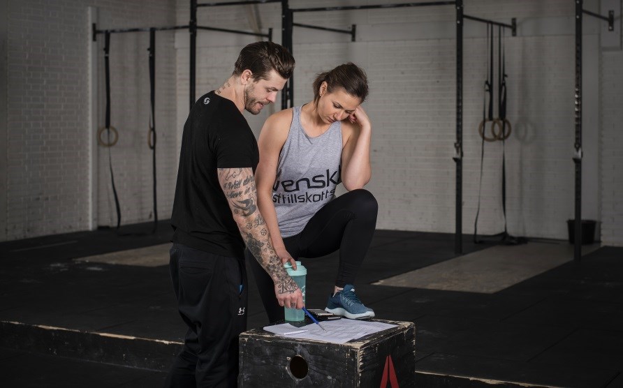 Man och kvinna i ett gym som tittar ned p ett papper.