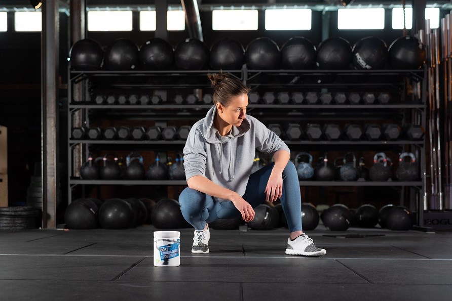 En tjej sitter på golvet på ett gym med en burk Core Endurance.