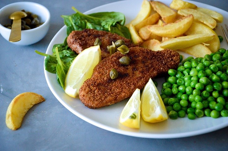 En tallrik med schnitzel, klyftpotatis och �rtor.