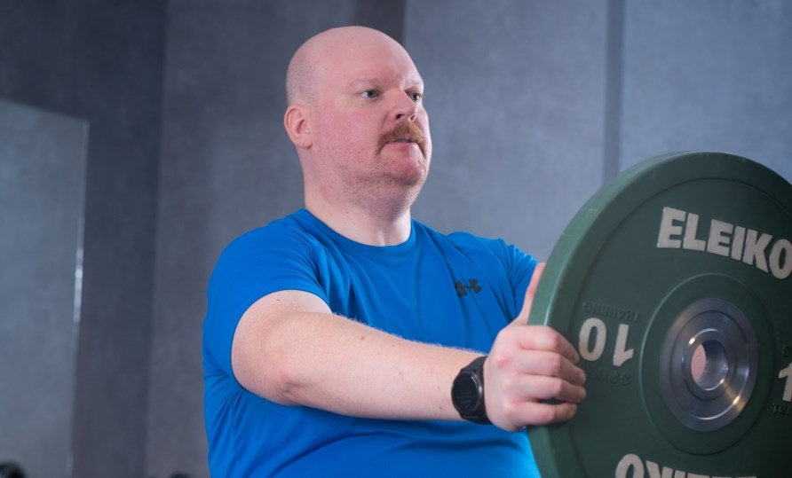 Man som trnar och hller i en viktplatta framfr sig.